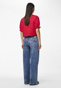 Blusa rossa corta con maniche a sbuffo, abbinata a jeans in denim azzurro chiaro oversize con finitura scolorita e vita alta.