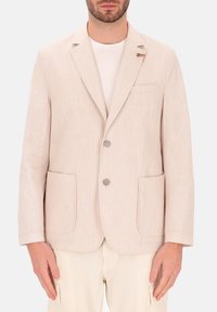 Blazer beige chiaro con righe verticali, chiusura a un bottone, rever a punta, due tasche frontali e una piccola spilla decorativa.