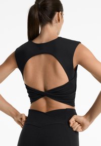 Top sportivo nero con un design intrecciato e corto sul retro. Tessuto liscio, maniche corte a cappuccio e apertura sulla schiena che rivela la pelle.