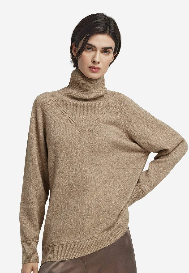 Beige polotröja med texturerad yta, med V-formad sömdetalj och lös passform. Ribbad mudd och nederkant fulländar designen.