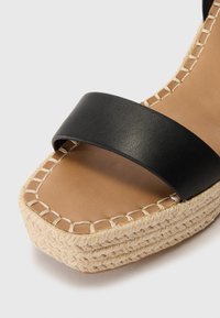 Espadrilové sandály s černým koženým popruhem, které mají tkanou jutu podešev, čtveratou špičku a béžovou stélku s kontrastním prošíváním.