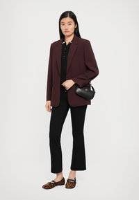 Burgundy blazer over a black polo, paired with black flared pants and leopard print flats; holding a small black handbag.