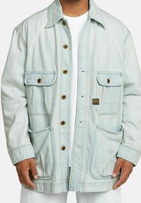 Ljusblå jeansjacka med avslappnad passform, som har fyra framfickor, bruna knappar och vita sömnadsdetaljer. Strukturerad tyg.
