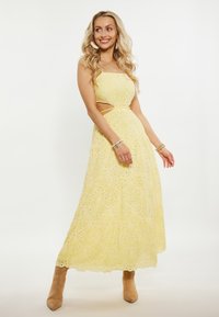 Rochie galbenă brodată cu detalii tăiate, având o siluetă fluidă și un model complex. Potrivită cu cizme până la glezne de culoare cămilă.