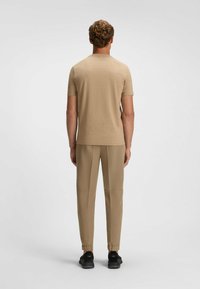 Beige T-Shirt mit kurzen Ärmeln, weicher Textur, kombiniert mit beigen, taillierten Hosen mit elastischen Bündchen und schwarzen Sportschuhen. Minimalistisches Design.