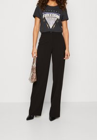 Pantalones de pierna ancha de talle alto en negro combinados con una camiseta gráfica oscura. El conjunto se complementa con un bolso de piel de serpiente y tacones negros.