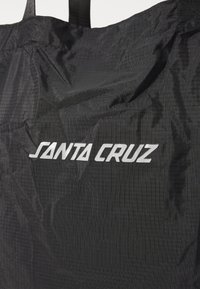 Črna najlon torba z teksturirano površino in belim logotipom "SANTA CRUZ" spredaj. Ima močne zgornje ročaje za enostavno prenašanje.