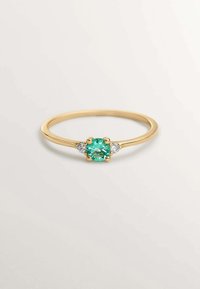 Anillo de oro con una gema redonda de turquesa en el centro, flanqueada por dos piedras claras más pequeñas, con una banda lisa y delgada.