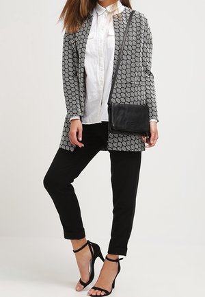 Cardigan lungo a motivo bianco e nero, camicia bianca con bottoni, pantaloni neri, borsa tracolla nera e sandali neri con tacco alto e cinturini.
