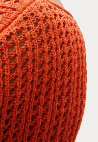 Oranje gebreide stof met een open gaaspatroon, die een gestructureerd, licht ontwerp laat zien met duidelijke verlengde steken.