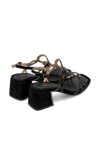 Zwarte blockhak sandalen met gekruiste banden, vervaardigd van een combinatie van gladde en gestructureerde materialen, en een beige accent rond de hak.