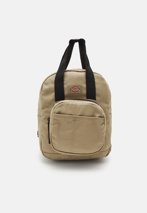 Kleine beige canvas rugzak met een voorste ritszak, zwarte handvatten en een Dickies logo patch aan de voorkant.