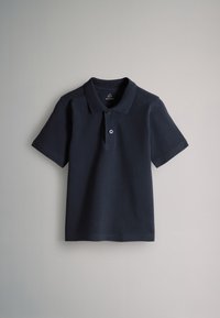 Polo bleu marine à manches courtes avec patte de boutonnage à deux boutons et col classique, posé à plat sur une surface gris clair.