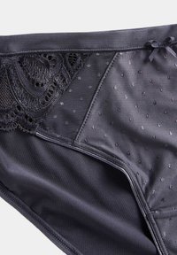 Zwarte onderbroek met een textuur van kant en een stippenpatroon, voorzien van een gladde stofafwerking en een klein strikje op de tailleband.