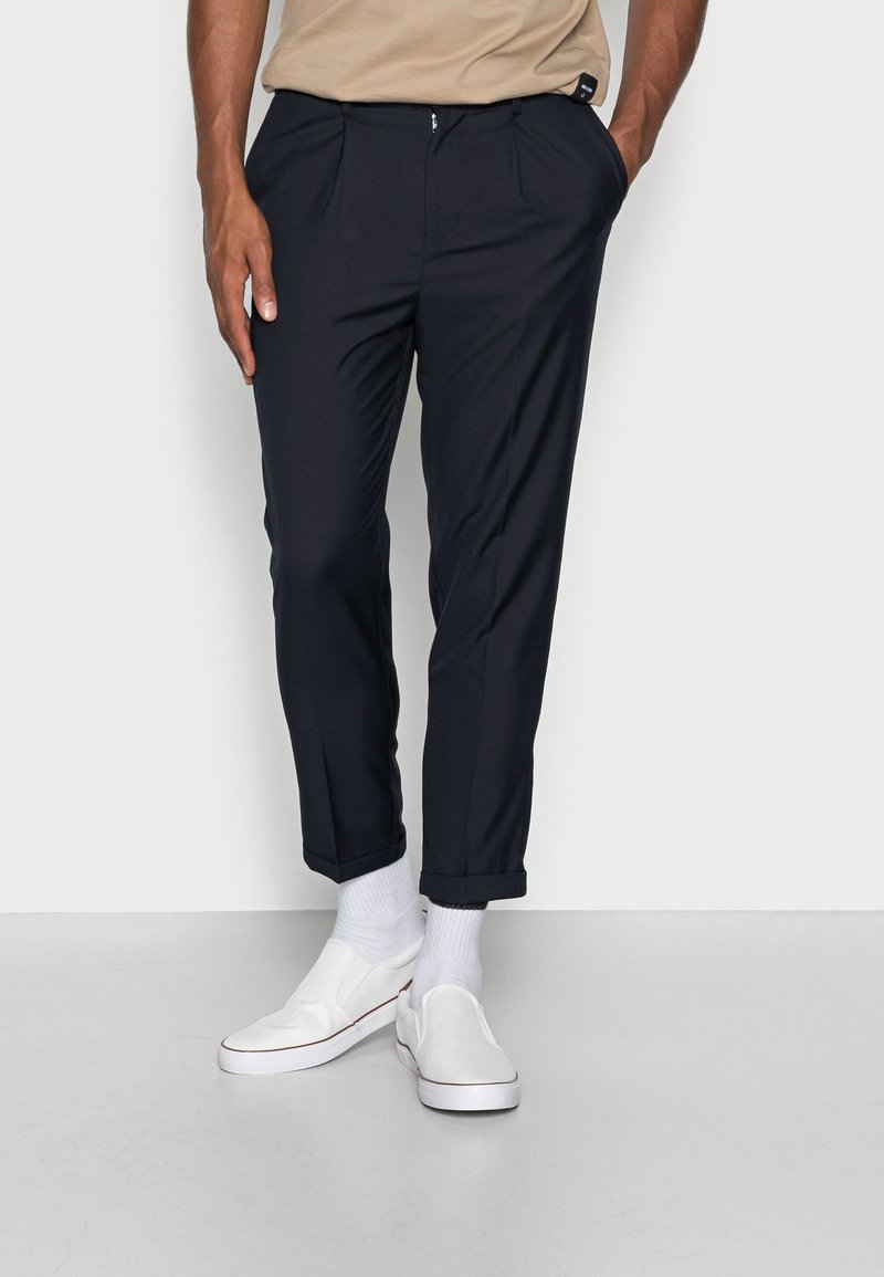 Námořnické, plisované kalhoty s tapered střihem, vyrobené z hladkého materiálu. Otočené manžety a nošeny s bílými slip-on botami a ponožkami.