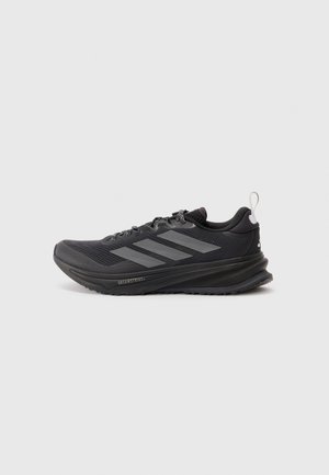 Scarpa sportiva nera con tomaia in rete, design con tre strisce grigie, collo imbottito, suola testurizzata e dettagli riflettenti.