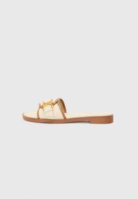 Beige slide sandal with a tan strap, gold hardware accent, and a flat sole. Fabric upper with a textured finish. Lightweight design.