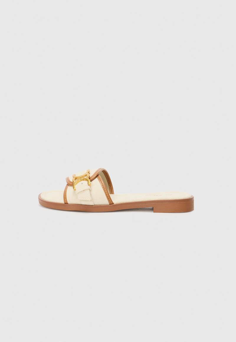 Beige Sandale mit einem braunen Riemen, goldenen Akzenten und einer flachen Sohle. Obermaterial aus Stoff mit strukturierter Oberfläche. Leichtes Design.