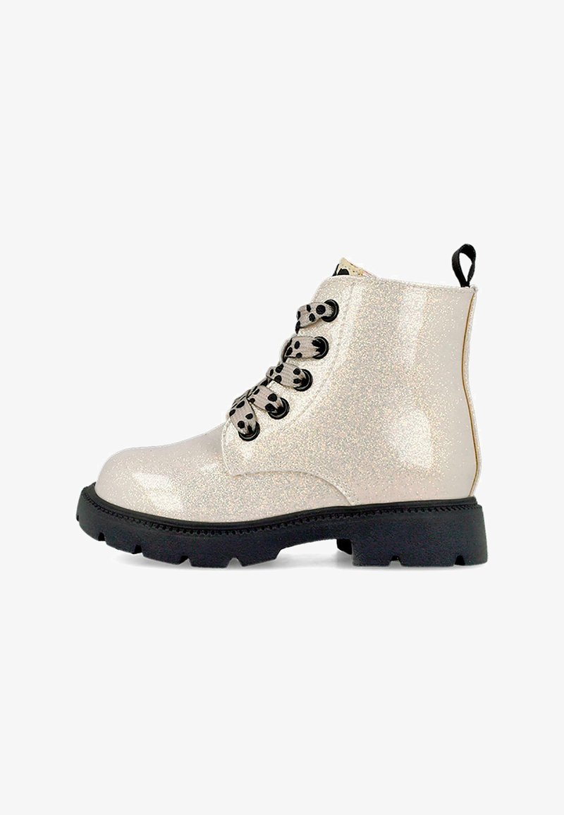 Botas de tobillo brillantes de color beis con cordones negros, suelas de goma y una lengüeta, que presentan un material brillante y un diseño robusto.