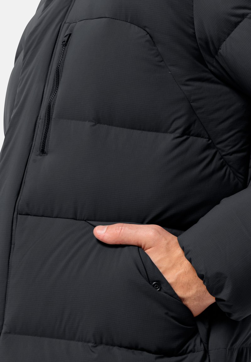 Schwarze Pufferjacke mit einer Reißverschlusstasche auf der Brust und einer seitlichen Handtasche. Der Stoff hat eine glatte, leicht strukturierte Oberfläche.