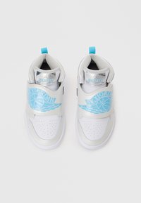 Baltas sporta apavi ar sudraba akcentiem, ar plašu siksnu ar zilo "SKYJORDAN" logotipu un perforētu purngali. Zila papēža cilpa vieglai uzvilkšanai.