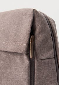 Γκρι υφασμάτινο σακίδιο με υφή, διαθέτει κλείσιμο με φερμουάρ και δερμάτινη λαβή για εύκολη πρόσβαση. Καθαροί γραμμές και μινιμαλιστικός σχεδιασμός.