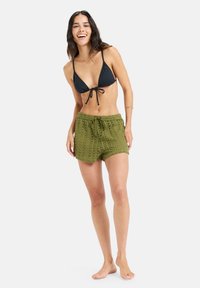 Čierny bikiny top s viazaním, doplnený olivovo zelenými pletenými šortkami so šnúrkou a textúrovaným vzorom. Modelka je bosá.