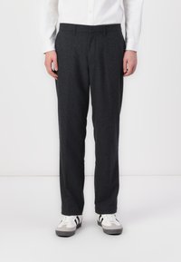 Pantalons en laine grise à coupe droite, avec un devant plat et des poches latérales. Portés avec des baskets blanches et grises.