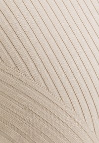 Beige gebreide stof met verticale geribbelde textuur, met een subtiel chevronpatroon. Zachte en gladde uitstraling, die de flexibiliteit van de stof benadrukt.