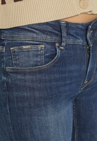 Mörkblå denimjeans med en klassisk femficksdesign. Har en liten logotypapplikation och subtil blekning, med kontrasterande sömmar.