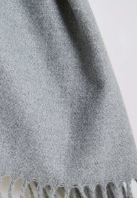 Écharpe tissée gris clair avec une texture douce, présentant des bords frangés et un motif chevrons subtil sur tout le tissu.