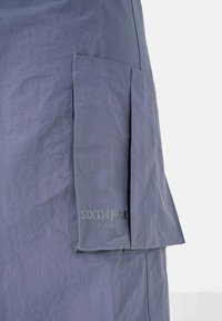 Grauer Stoffrock mit einer seitlichen Tasche, mit genähten Details und einem aufgedruckten Logo "SIXTH JUNE PARIS" in dezenten Buchstaben.