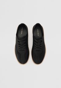 Baskets en mesh noir avec un design respirant, fermeture à lacets à l'avant et une semelle extérieure en caoutchouc marron clair. L'intérieur comprend une semelle intérieure de marque.