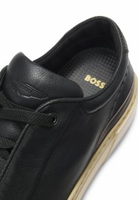 Black leather sneaker featuring a smooth texture, round toe, and contrasting off-white rubber sole. Details include laces and embossed logo.