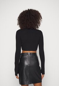 Maglione nero corto con maniche lunghe abbinato a una gonna in pelle nera a vita alta con zip centrale sul retro. Tessuto morbido.