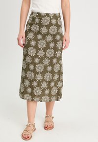 Jupe midi vert olive avec des motifs floraux blancs, en tissu léger et silhouette droite. Associée à des sandales à lanières dorées.