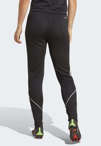 Schwarze Sporthose mit taillierter Passform, elastischem Bund und weißen Akzentstreifen an den Seiten. Dazu werden schwarze und grüne Fußballschuhe getragen.