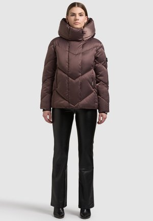 Brun vadderad jacka med hög krage och sikksakkmönster, med en glansig finish och detaljer med zipfickor, kombinerad med svarta utsvängda byxor.