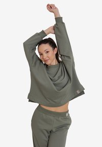 Zielona bluza i dopasowane spodnie, obie z miękkiego materiału. Oversize'owa góra ma okrągły dekolt i akcent logo na dolnym krawędzi.