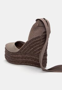 Espadrilles a zeppa marroni con tomaia in tessuto texturizzato e dettagli in corda intrecciata. Presentano una punta arrotondata e una fascia di chiusura marrone sul retro.