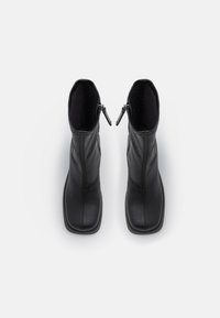 Paire de bottes en cuir noir mi-mollet avec bouts carrés et fermetures éclair latérales, vue de dessus sur fond blanc.