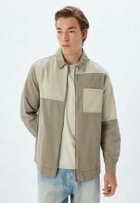 Lichtgewicht, bicolor jas in beige en khaki, met een ritssluiting aan de voorkant, puntkraag, borstzak en een losse pasvorm. Glad katoenmix materiaal.