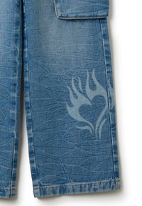 Pantalones de mezclilla en un tono azul desgastado, con patrones texturizados y un sutil diseño de corazón en llamas en la parte inferior de la pierna, junto con un detalle de bolsillo.