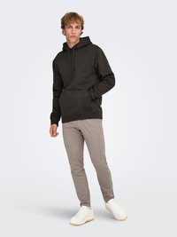 Sweat-shirt noir à capuche avec poche avant, pantalon gris ajusté et baskets blanches avec semelles texturées. Design simple, look décontracté.