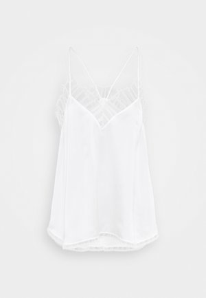 Hvit cami med v-halsdesign, tynne stropper, teksturerte blonder ved skuldrene og en buet nederkant. Glatt stofftekstur.