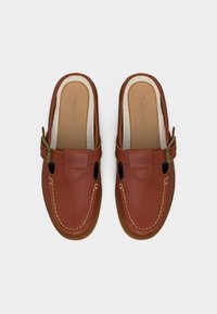 Mocassins marron en cuir à enfiler avec des brides à boucle et des coutures visibles, vus de dessus sur un fond blanc.