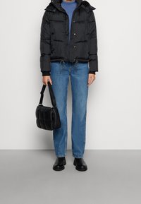 Chaqueta acolchada negra con capucha, cierre de cremallera y cintura con cordón, combinada con jeans rectos azul claro y un pequeño bolso negro.