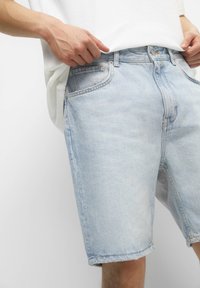 Vaaleansiniset farkkushortsit, joissa on rento leikkaus, edessä taskut ja raaka helma. Materiaalissa on kevyttä haalistumista kuluneen ilmeen aikaansaamiseksi.