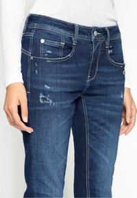 Mörkblå denimjeans med en urblekt yta, slitna detaljer, femficksdesign och silverdetaljer vid midjan och fickorna.