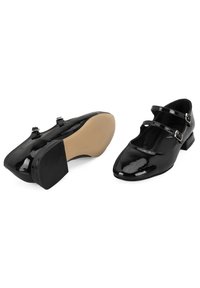 Zwarte gepatineerde leren schoenen met een spitse neus, verstelbare dubbele banden en een lage blokhak. De zool is beige en gestructureerd voor grip.